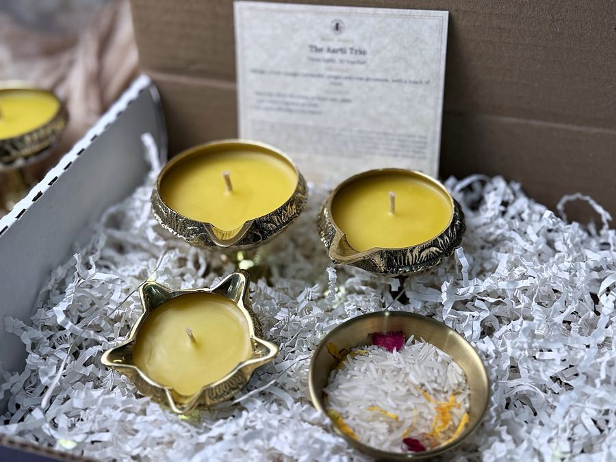 Three brass diyas poured with beeswax and a brass katori of rice in a gift box