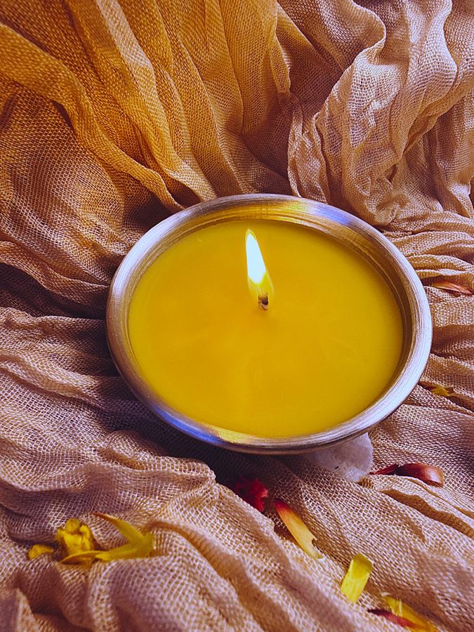 Beeswax candle lit in a stainless steel katori