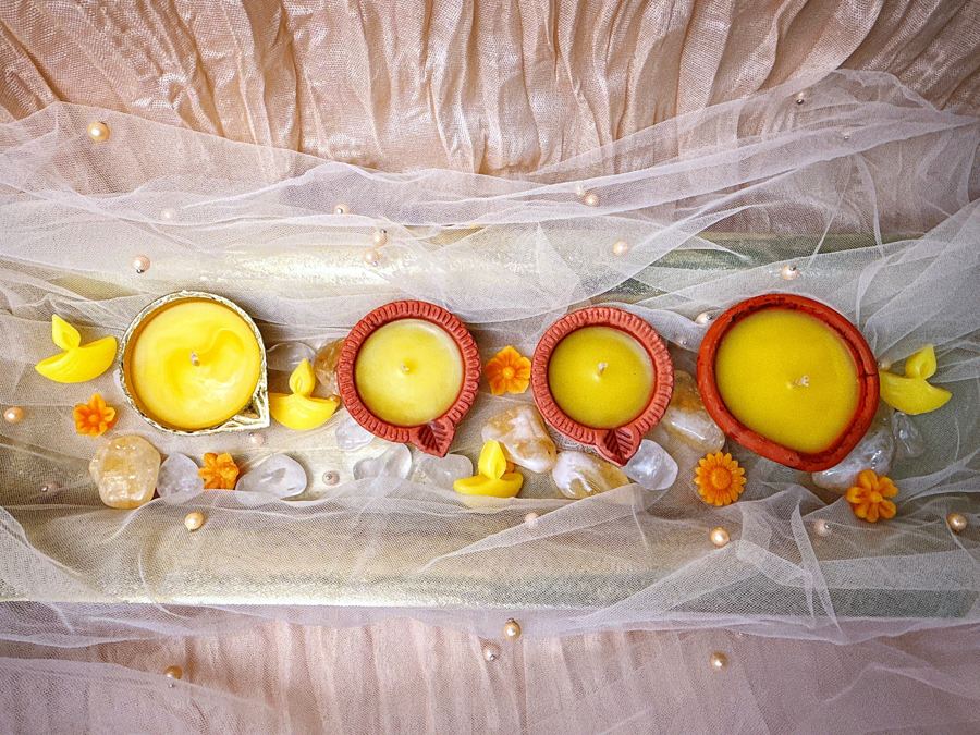 A row of clay and brass diyas with marigolds on a white cloth